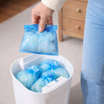 Person holding a fully sealed diaper, more inside a DiaperSealer bin in the background.