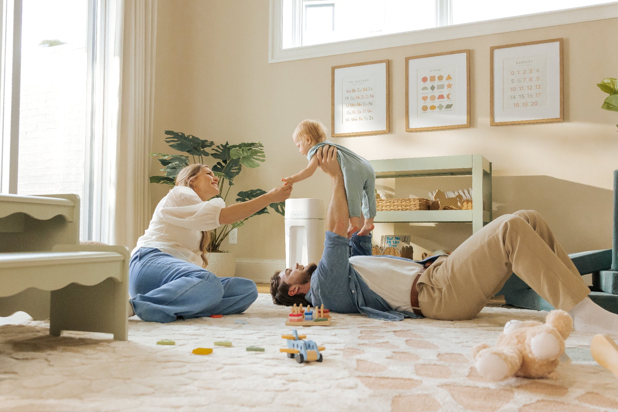 Family playing on the floor with toys in a bright nursery. DiaperSealer in the background.