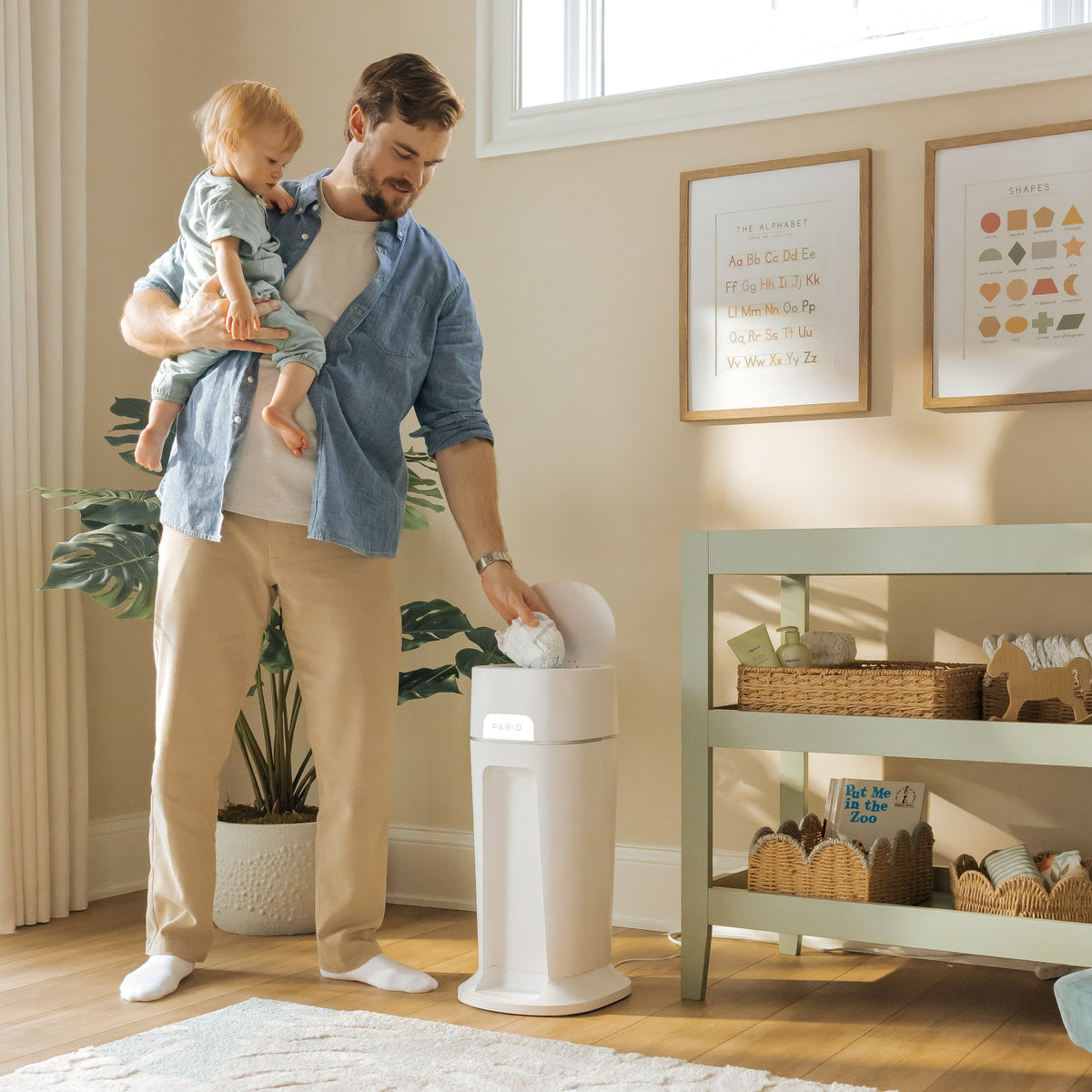 Man holding a baby in a nursery, disposing of a diaper in DiaperSealer station.