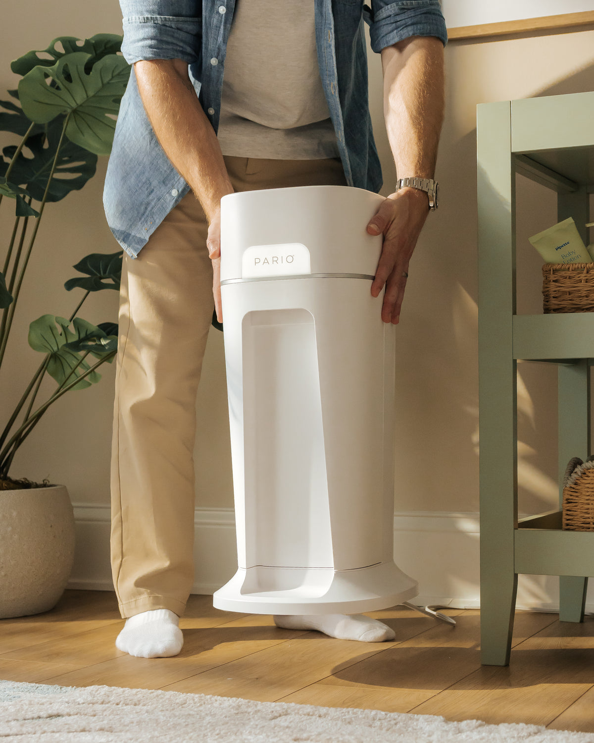 Man placing DiaperSealer in nursery setting, beside shelves and plants.