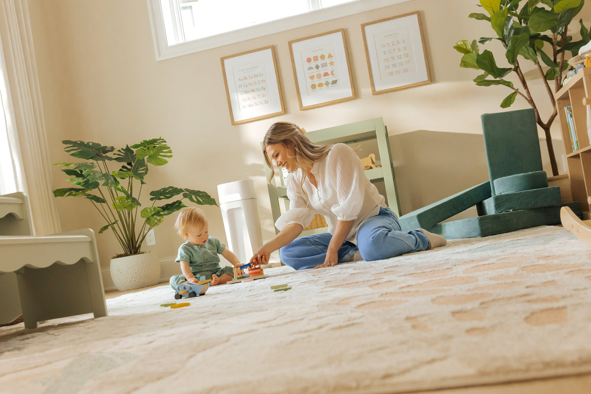 Woman and child playing on a rug in a bright bedroom. Diaper Sealer in the background.